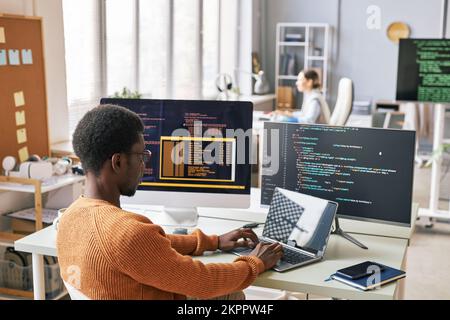 Young man in warm sweater coding on laptop in office of IT company Stock Photo