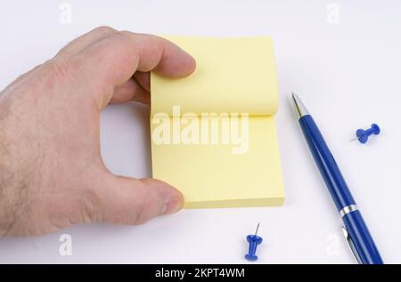 A man's hand flips through the note paper. On the table are paper, buttons and a pen. Stock Photo