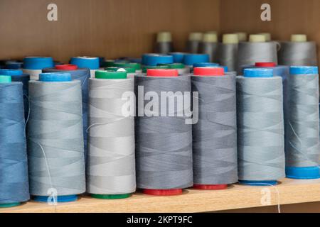 Sewing thread cones of different shade of colors on shelf in sewing studio closeup Stock Photo