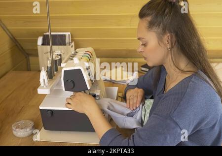 A woman designer works on an overlock sewing machine on tailoring. Small tailoring business. Stock Photo