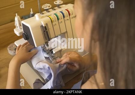 A woman designer works on an overlock sewing machine on tailoring. Close-up. Small tailoring business. Stock Photo