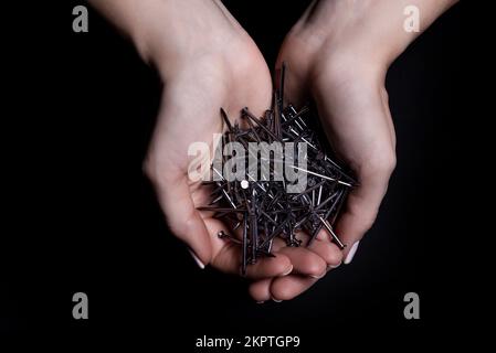 Woman's hands holding screws and dowels in palms. Isolated on black. female hands hold screws nails washers nuts on a black background Stock Photo