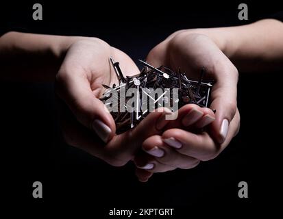 Woman's hands holding screws and dowels in palms. Isolated on black. female hands hold screws nails washers nuts on a black background Stock Photo