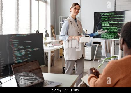 Female developer with prosthetic arm pointing at programming code for VR videogame Stock Photo