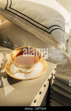 Black tea in fancy gold and white teacup in afternoon on bedside table Stock Photo