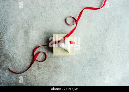 Overhead view of a white gift box tied with a red ribbon and decorated with a ceramic heart ornament Stock Photo