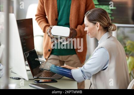 Smiling female software developer pointing at laptop screen when discussing features with project manager Stock Photo