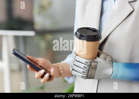 Closeup image of woman with prosthetic arm holding cup of take out coffee and checking notifications on smartphone Stock Photo