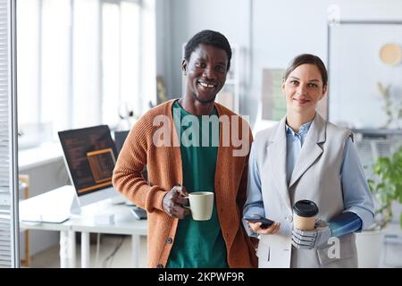 Portrait of positive business people with cups of coffee standing in office of IT company Stock Photo