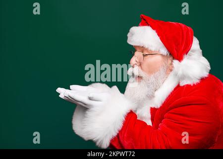 Winter December sale discount black friday. Profile side view aged Santa in costume blow on open palms hand near face pouted lips isolated on shine Stock Photo