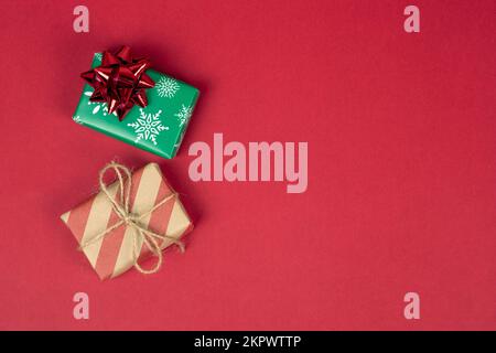 Two christmas and new year presents or gifts on red background with copy space, top view. Gift boxes wrapped in green and craft red paper with bows Stock Photo