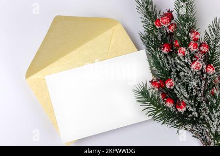 Christmas letter mock up with an empty blank white sheet of paper or card and a golden envelope on white background and a christmas tree branch and Stock Photo