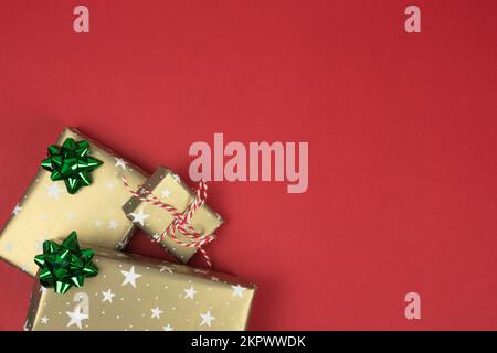 A pile of wrapped christmas presents and gift boxes in golden paper top view on red background with stars and copy space. Stock Photo
