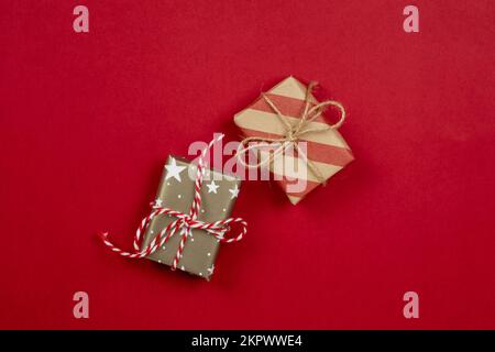 Two wrapped christmas presents and gift boxes wrapped in craft paper top view on red background with stripes and stars and copy space. Stock Photo