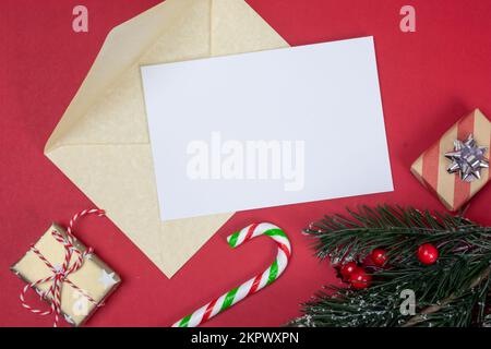 Christmas letter mock up with golden envelope and blank empty white paper page with copy space top view. Fir tree branch, holly, gold colour presents Stock Photo