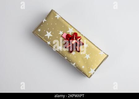 One wrapped present in golden paper with red bow top view on grey or white background and copy space . Stock Photo
