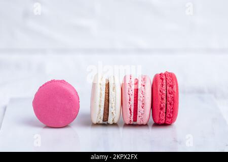 Close up of Macaroons in different colours on bright white background with subtle reflection on marble tray. Popular merengue dessert with filling ins Stock Photo