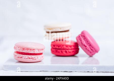 Close up of Macaroons in different colours on bright white background with subtle reflection on marble tray. Popular merengue dessert with filling ins Stock Photo