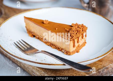 A piece of caramel cheesecake with cookie crumbs on top. Creamy three layer cake on bright plate. Popular American dessert. Stock Photo