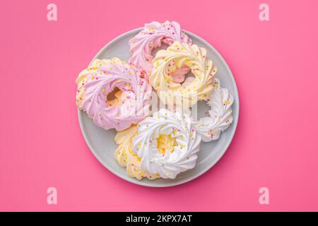 Different colors meringues with sprinkles on the plate on pink table. Top view. Stock Photo