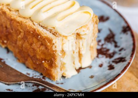 French dessert called Mille Feuille or Napoleon cake on rustic wooden board. Layered tasty cake with vanilla cream and puff pastry. Stock Photo