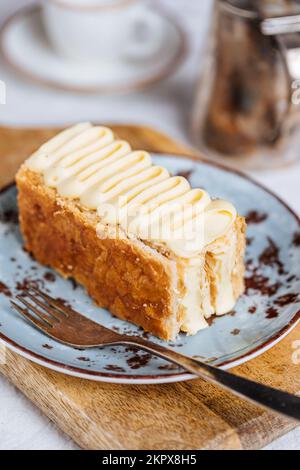 French dessert called Mille Feuille or Napoleon cake on rustic wooden board. Layered tasty cake with vanilla cream and puff pastry. Stock Photo