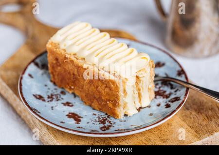 French dessert called Mille Feuille or Napoleon cake on rustic wooden board. Layered tasty cake with vanilla cream and puff pastry. Stock Photo