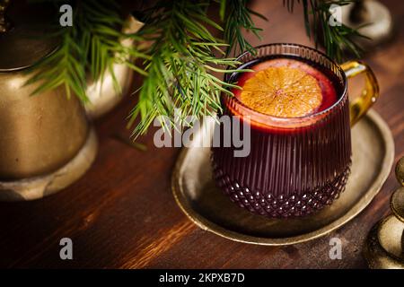 Mulled wine with cinnamon and orange served in festive Christmas decoration on wooden board. Party and New Year atmosphere. Christmas tree in backgrou Stock Photo