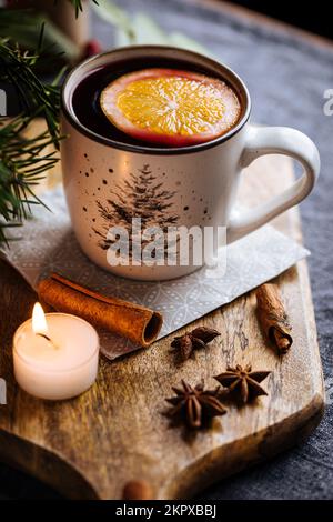 Mulled wine with cinnamon and orange served in festive Christmas decoration on wooden board. Party and New Year atmosphere. Christmas tree in backgrou Stock Photo