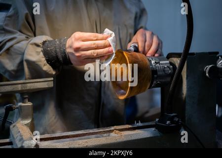 Professional carpenter oiling finished wooden bowl on wood lathe Stock Photo