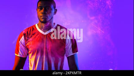 Portrait of serious african american male soccer player in red jersey standing on violet background Stock Photo