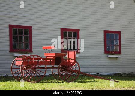 Red antique wagon in front of old white barn. Stock Photo