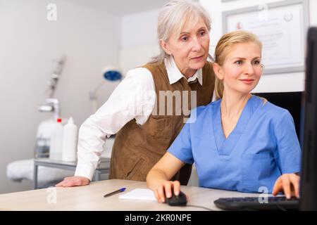 Interested elderly female client with cosmetologist looking at computer screen Stock Photo