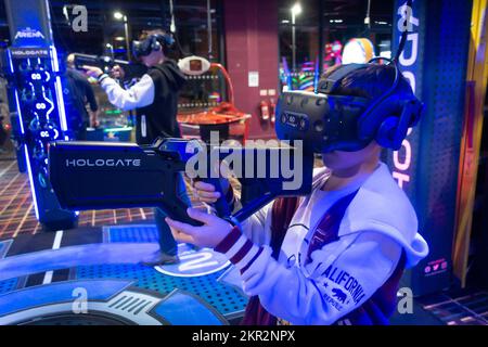 A boy playing a virtual reality video game in an arcade, holding a gun and wearing a VR headset Stock Photo
