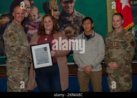 Taylor Winborn (middle left) receives a Volunteer of the Quarter Award from Maj. Gen. John Meyer III (left), commanding general of the 1st Infantry Division and Fort Riley, and Command Sgt. Maj. Christopher Mullinax (right), the command sergeant major of the 1st Inf. Div. and Fort Riley, Nov. 7, 2022, at Victory Hall in Fort Riley, Kansas. Winborn received the award for her volunteer work with the 5th Squadron, 4th Cavalry Regiment's Soldier Family Readiness Group. Stock Photo