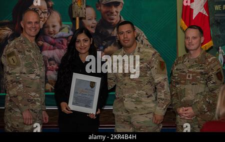 Guadalupe Castillo (middle left) receives a Volunteer of the Quarter Award from Maj. Gen. John Meyer III (left), commanding general of the 1st Infantry Division and Fort Riley, and Command Sgt. Maj. Christopher Mullinax (right), the command sergeant major of the 1st Inf. Div. and Fort Riley, Nov. 7, 2022, at Victory Hall in Fort Riley, Kansas. Castillo received the award for her work in her company's Soldier Family Readiness Group. Stock Photo