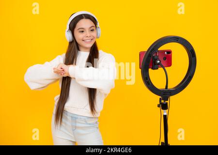 Music kids blog. Blogging, videoblog. Teenager child blogger with phone recording video on isolated yellow studio background. Influencer teen girl Stock Photo