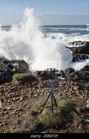 An iPhone on a small tripod captures footage of huge waves during a king tide on the rocky shore in Yachats, Oregon. Stock Photo