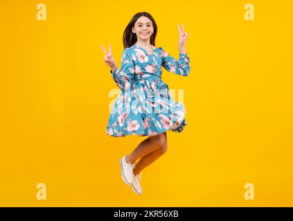 Full size photo of positive teen girl jump with movement summer dress, fashion kids outfit isolated over yellow background. Stock Photo