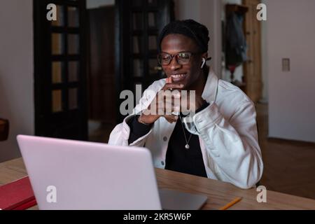 Young smiling happy African man remote worker in eyewear looking at laptop screen reading e-mail Stock Photo