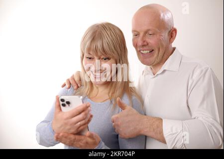 Happy retired family couple using mobile phone for video call together, talking to relations, getting good news, having fun smiling and laughing. Carefree mature pensioners chatting online on cell Stock Photo