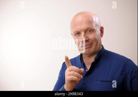 Emotions of an adult handsome bald man The man smiles slyly and looks into the frame. He shows a thumbs up as if for some reason he wants to draw attention. Stock Photo