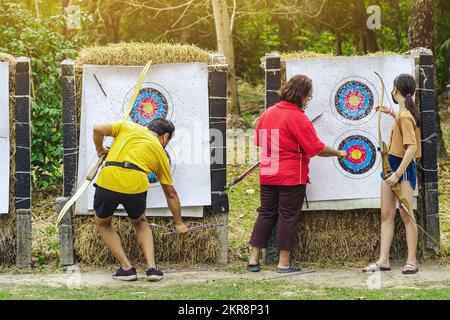 Back view of female officer wear face mask collect arrows fired from a bow on sport target. Woman clearing arrows from target to start new game. Medit Stock Photo