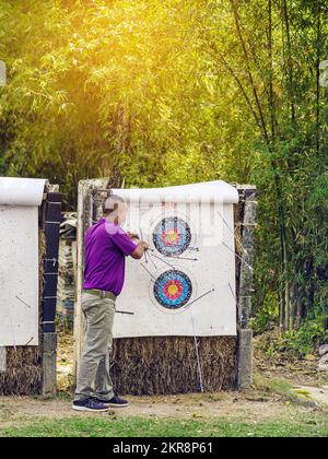 Back view of male officer wear face mask collect arrows fired from a bow on sport target. Archer clearing arrows from target to start new game. Medita Stock Photo