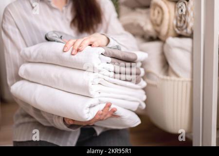 Beautiful woman in winter thick warm robe is sitting and neatly folding bed linens and bath towels Stock Photo