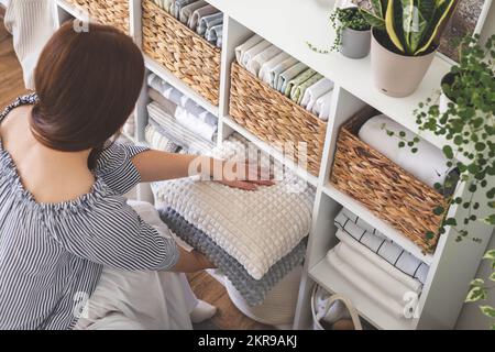 Modern housewife putting neatly folded towels, pillowcases, duvet covers into wicker natural eco-friendly basket Stock Photo