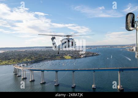 221111-N-EV253-1131 SAN DIEGO (Nov. 11, 2022) – An MH-60S Knighthawk helicopter, assigned to the 'Merlins' of Helicopter Sea Combat Squadron (HSC) 3, flies over the Coronado Bridge before participating in a commemorative flyover of the Nimitz-class aircraft carrier USS Abraham Lincoln (CVN 72) during the Armed Forces Classic, Carrier Edition 2022. During the event, which was held on Veterans Day, a basketball court was constructed on Lincoln's flight deck, and the Gonzaga Bulldogs played against the Michigan State Spartans. HSC-3 is the Navy's West Coast MH-60S fleet replacement squadron, resp Stock Photo