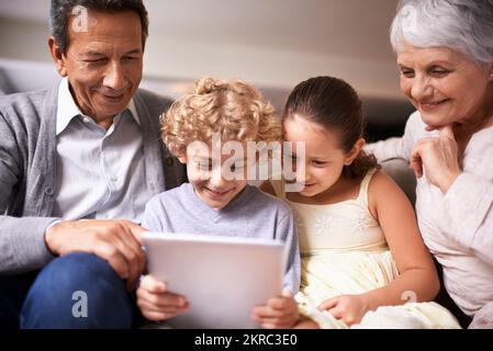 Showing granny and gramps the latest tech. A shot of two kids and their grandparents using a digital tablet while sitting on the sofa. Stock Photo