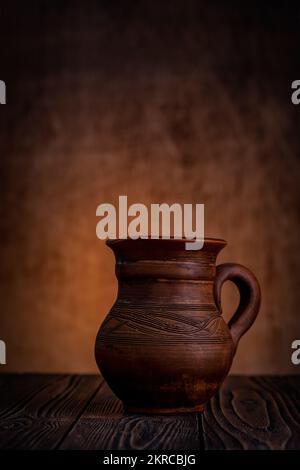 Clay jug on a dark background on a wooden table. Stock Photo