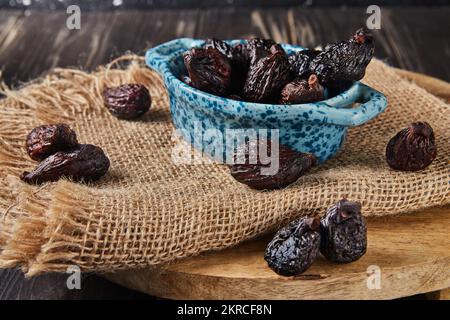 Dried mission figs in glass bowl on burlap and wooden background. Stock Photo